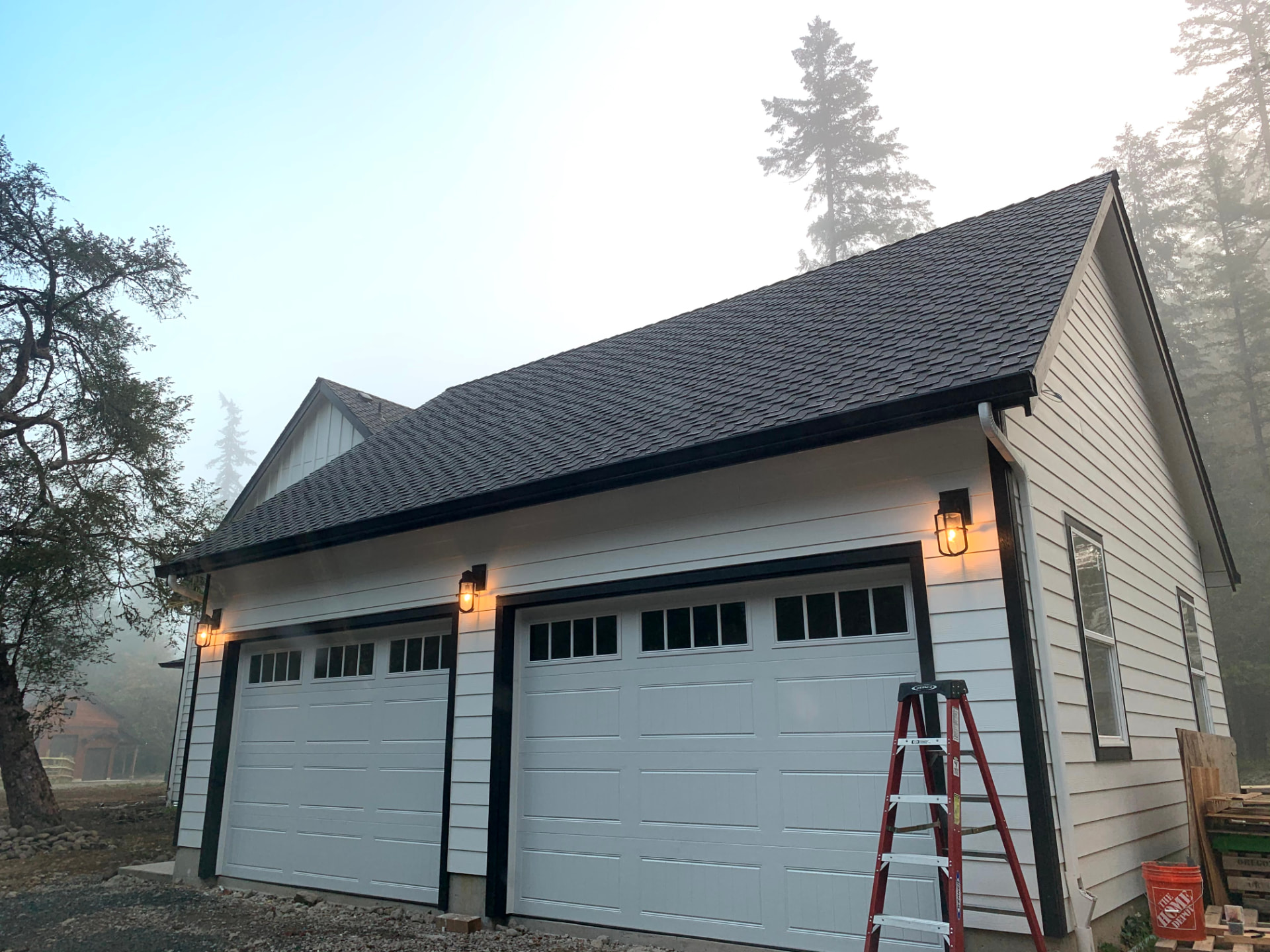 Exterior garage with lit carriage lights on a foggy evening